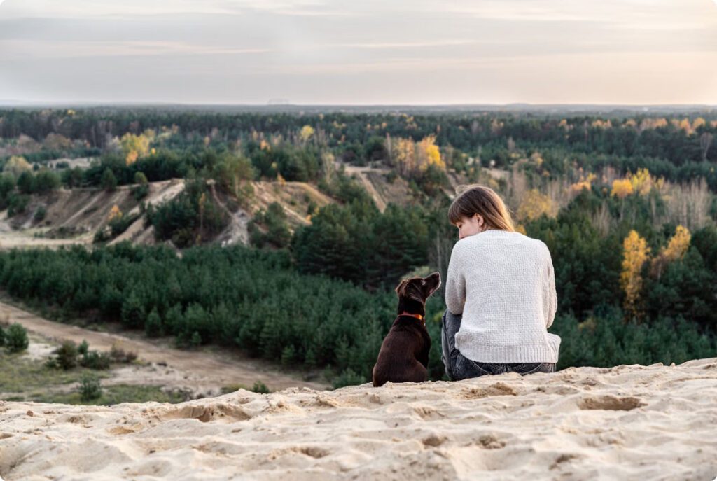 Person with a white sweater sitting on a ledge with a black dog.